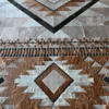 Luxury designer rug features geometric diamond and triangle patterns in brown, tan, and gray hide.