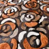 Close-up of luxury designer hide rug, featuring swirling rose-like patterns in brown, orange, black, and white with a high-end textured finish.