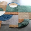 Luxury designer hide rug with geometric patterns in green, beige, blue, and brown on a concrete floor.