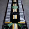 A luxury designer rug with geometric patterns in green, gold, and black on gray handmade fur strips.