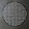 Luxury designer round rug in black and white houndstooth on gray concrete floor.