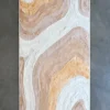 Luxury designer bath mat with rounded corners and an abstract beige, tan, and white pattern on a gray floor.