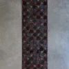 Luxury designer rug with red geometric pattern on dark ground, displayed on gray floor.