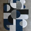 Luxury designer wool rug with geometric blue, black, gray, and white shapes on concrete floor.