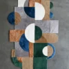 Luxury designer rug with abstract shapes in green, blue, tan and gray on a gray floor.