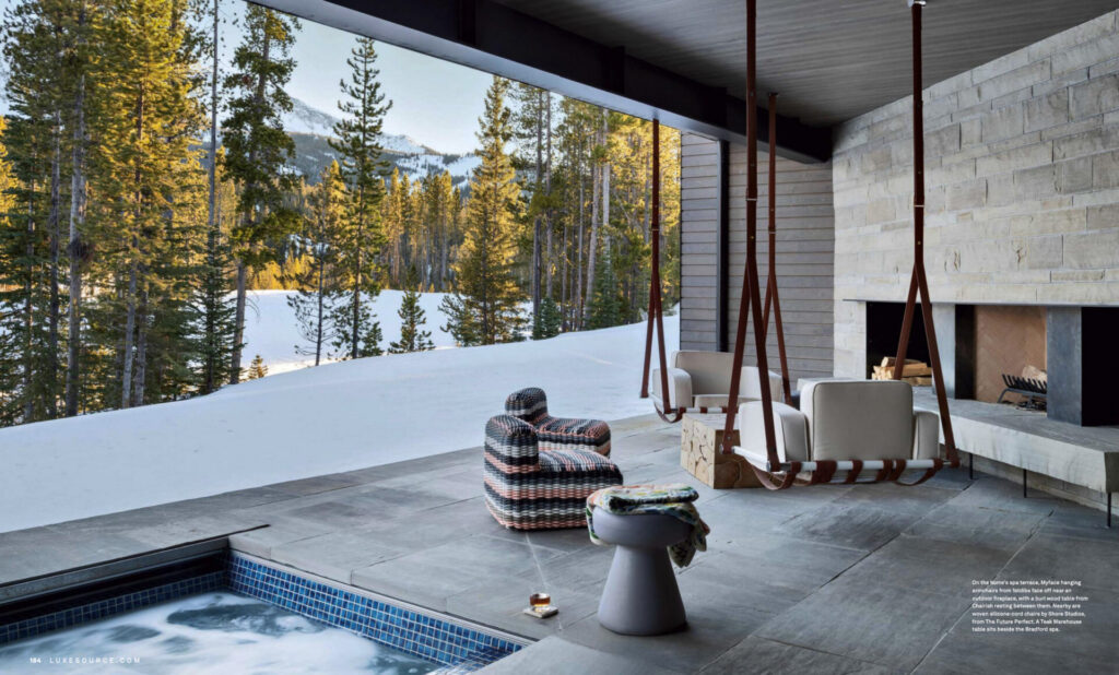 A modern patio with lounge chairs and a luxury designer rug, overlooking snowy mountains through large open windows.