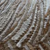Luxury designer rug features a close-up of wavy, striped handmade hide texture in brown, gray, and white.