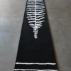 Luxury designer wool rug, black with white leaf pattern, on sleek gray flooring.