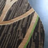 Curved edge of a luxury designer rug with brown, tan, and green branch-like lines on gray flooring.