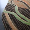 A close-up of a luxury designer rug with an abstract brown, orange, and green pattern on a gray floor.