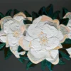 Three large white embroidered flowers and green leaves on a dark luxury designer rug background.