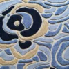 Close-up of a luxury designer rug with textured wool and silk, featuring an abstract floral pattern in blue, beige, and navy tones.