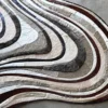 Luxury designer rug with abstract, wavy rings in brown, gray, cream, and white on a concrete floor.