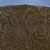 Luxury designer rug close-up featuring textured brown wool with an abstract raised swirl pattern on a gray background.