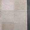 Close-up of a luxury designer rug: 3 Lock Box Hide 15204, light beige patchwork, plush handmade hide texture on dark gray floor.