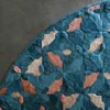 A round luxury designer rug, Fez Hide 28129, with a geometric pattern in teal, peach, and beige on a dark gray floor.