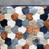 The Leigh Hide 27210 designer rug displays luxury handmade hide patchwork in blue, brown, beige, gray, and white on a gray floor.