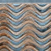 This luxury designer rug showcases wavy stripes in brown, tan, blue, and gray on a dark floor.