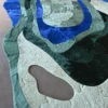 Luxury designer rug features abstract blue, green, and beige shapes on handmade hide.