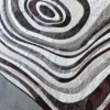 Luxury designer rug with curved gray, brown, and white bands on concrete floor.