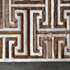 Luxury designer rug with geometric maze, brown and tan handmade hide strips on gray floor.