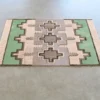 Luxury handmade designer rug with geometric beige, gray, and green pattern on light floor.