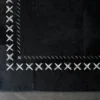 Close-up of Custom Hide 28620 luxury designer rug with bold white cross-stitching on a gray floor.