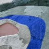 Close-up of luxury custom designer rug: layered faux fur in blue, green, white, and gray with an irregular pink accent.