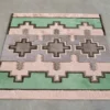Luxury custom rug with geometric design in pastel pink, green, and gray on light gray floor.