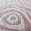 Close-up of a luxury designer rug with soft pink and gray concentric patterns, inspired by handmade wool rugs.