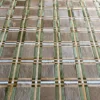 Close-up of a luxury designer rug with a green, gold, and white grid on brown hide.