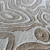 Close-up of luxury designer rug, handmade silk and wool, with textured beige lines echoing topographic detail.