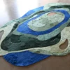Luxury designer rug with abstract blue, green, and beige patterns on a polished floor.