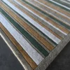 Close-up of Jet Stream Wool 15357 luxury designer rug with green, brown, and gray stripes on a dark floor.