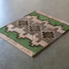Luxury designer rug—square textile with green, beige, and brown geometric crosses.