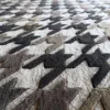 Close-up of luxury designer rug fabric with a textured houndstooth pattern in black, brown, gray, and beige.