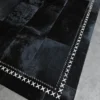 Luxury designer dark patchwork hide rug with white cross-stitched border on concrete floor.