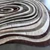 Close-up of a luxury designer oval rug with brown, gray, and white concentric rings on a smooth gray floor.