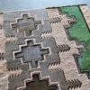 A close-up of a high end designer rug, featuring geometric patterns in gray, beige, and green hide.