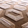 Luxury custom handmade silk and wool rug with raised geometric patterns on textured brown surface.