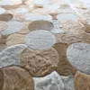 Overlapping luxury custom hide designer rugs in beige, brown, and gray with varied textures cover the floor.