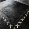 Close-up of luxury designer hide rug in black patchwork, bold white stitching, high end finish.