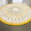 Luxury designer round hide rug with radiating yellow and green lines on gray floor.