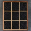 Luxury designer rug panel, nine-square wooden grid with dark handmade hide rug insets, set against a gray concrete wall.