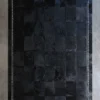 Luxury designer black patchwork rug with white stitched border on concrete floor.
