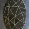 Luxury designer oval rug with silver curves on a dark textured background, displayed on a smooth gray floor.