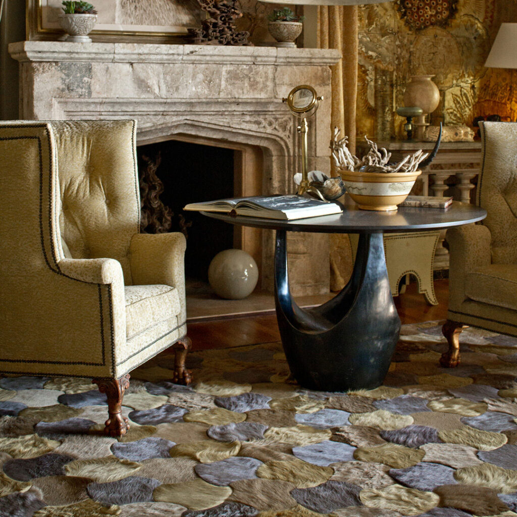 Two armchairs face a round black table on a luxury designer rug by the stone fireplace.